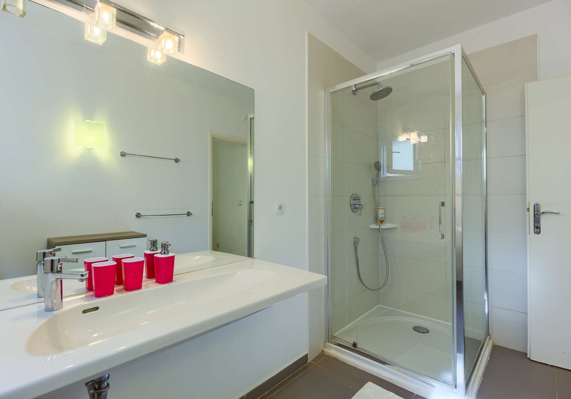 A modern bathroom with a glass-enclosed shower, a white sink, and a mirror with lights above it.