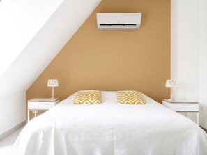 Experience comfort and style in this cozy bedroom with a sloped ceiling, featuring a plush bed, bedside tables, and a warm beige tone.