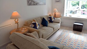 A cozy living room with a beige sofa, two side tables with lamps, a colorful rug, and a window with a view of greenery. - Valley Retreat - Peaceful Cottage, Walk to Beach (Saundersfoot)