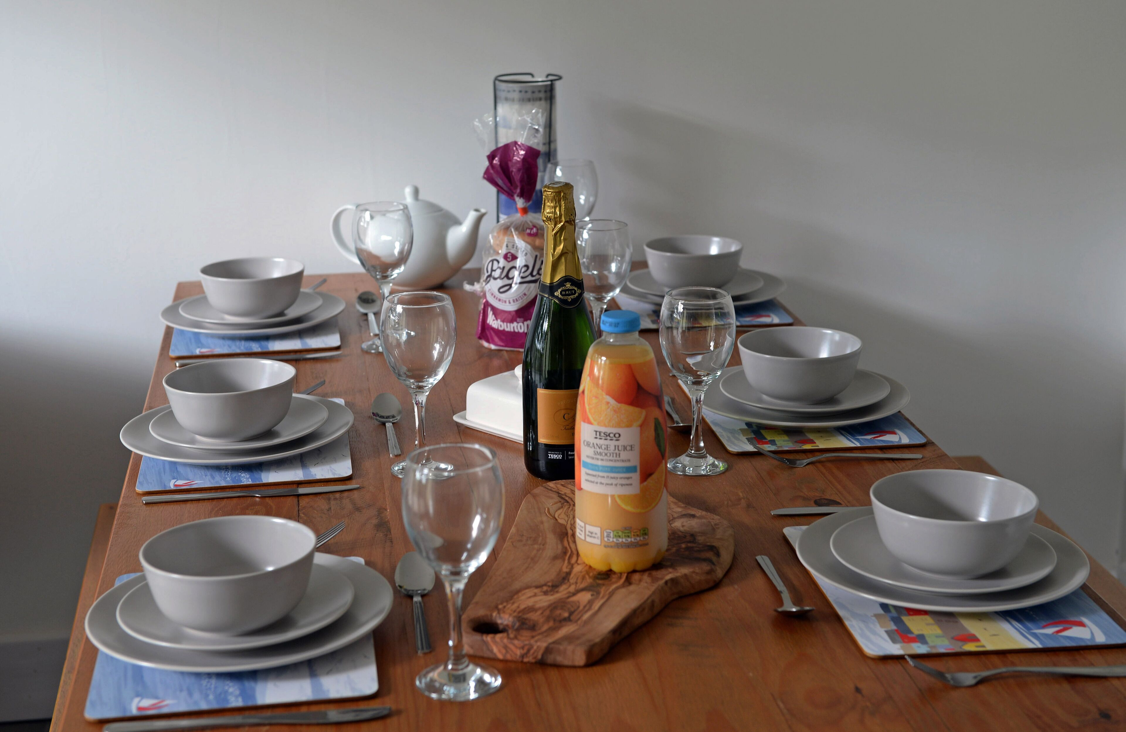 Een eettafel gedekt met meerdere kommen, wijnkleden en een fles sinaasappelsap.