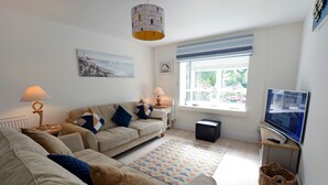 A living room with a sofa, two lamps, a TV, and a window with a view of greenery. - Valley Retreat - Peaceful Cottage, Walk to Beach (Saundersfoot)