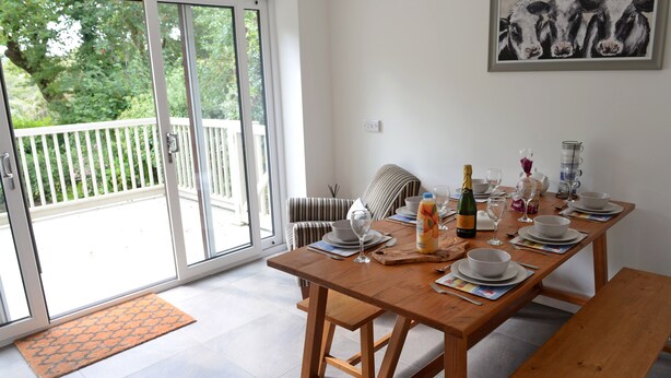 A dining area with a wooden table set for four, a bench, and a sliding glass door leading to a balcony. - Valley Retreat - Peaceful Cottage, Walk to Beach (Saundersfoot)