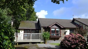 A two-story house with a front porch, a stone chimney, and a large bush. - Valley Retreat - Peaceful Cottage, Walk to Beach (Saundersfoot)