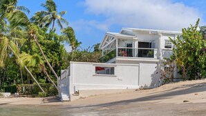 Een pand aan het strand met een wit gebouw, een balkon met uitzicht op de oceaan en palmbomen op de achtergrond.