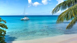 Een heldere turquoise zee met een zeilboot voor anker vlakbij de kust, omringd door palmbomen.