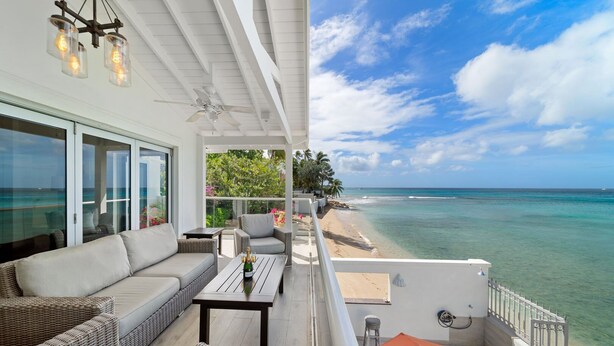 Een balkon met rieten meubels, een tafel met een fles en uitzicht op de oceaan.