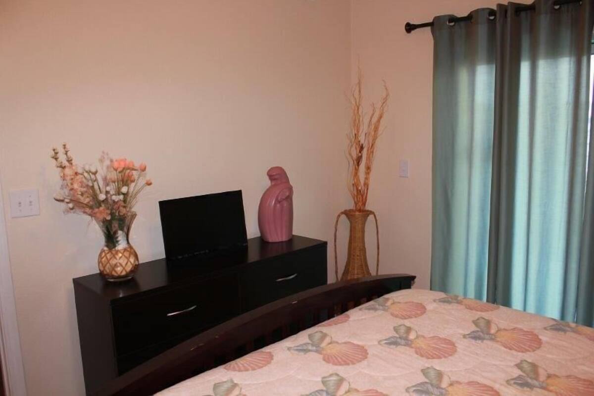 Une chambre à coucher avec un lit, une commode, un vase de fleurs et un téléviseur posé sur la commode.