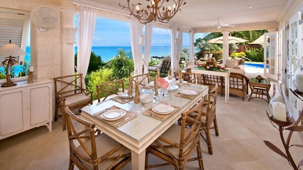 A dining area with a view of the ocean, a chandelier, wicker furniture, and a pool.