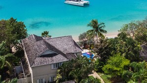 A coastal property with a large house, a beach, and a sailboat in the water.