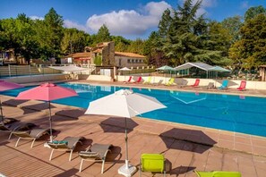 Un espace piscine doté de chaises longues et de parasols, entouré d’arbres et d’immeubles.