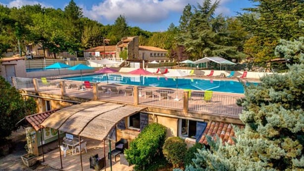 Un espace piscine comprenant plusieurs zones, notamment une piscine principale et des piscines plus petites, le tout entouré d’arbres et de bâtiments.