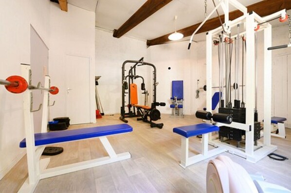 Un gimnasio con equipo de levantamiento de pesas, bancos y una pared azul.