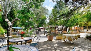 Un espace extérieur aménagé en terrasse, avec des tables et des chaises, entouré de plantes en pot et d’arbres.
