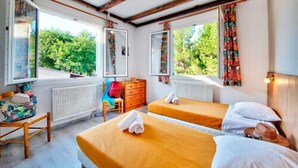 Une chambre avec deux lits, une chaise en bois, une commode et une fenêtre donnant sur un paysage verdoyant.