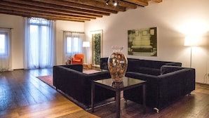 A living room with a dark sofa set, a glass coffee table, and a large vase. There is a wooden ceiling with exposed beams, a red rug, and a lamp. - Relais Villa Ormaneto (Cerea)