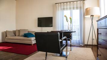Una sala moderna con un sofá, una silla negra, un televisor, una lámpara y un ventanal con cortinas.