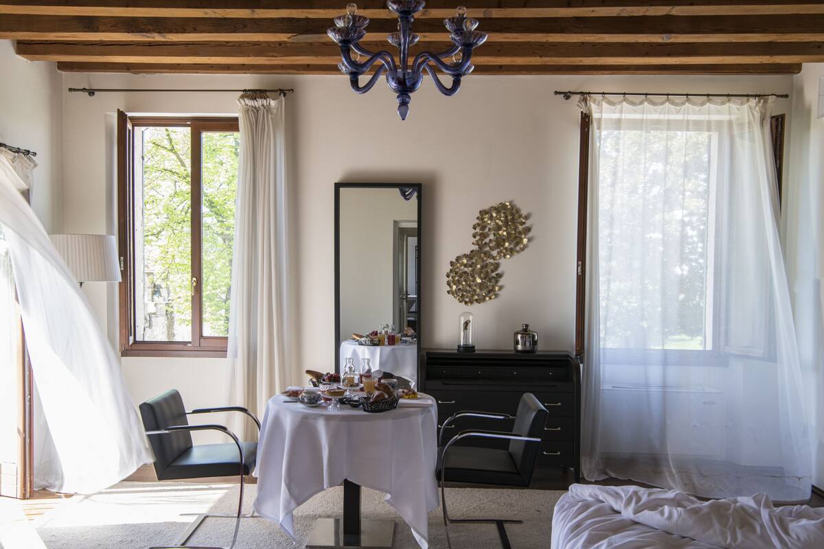 A room with a bed, a table with breakfast items, a dresser, and a chandelier.