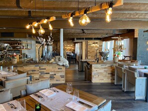 A restaurant with wooden tables and chairs, a bar area, and hanging light fixtures. - Hotel Twing (Hasliberg)