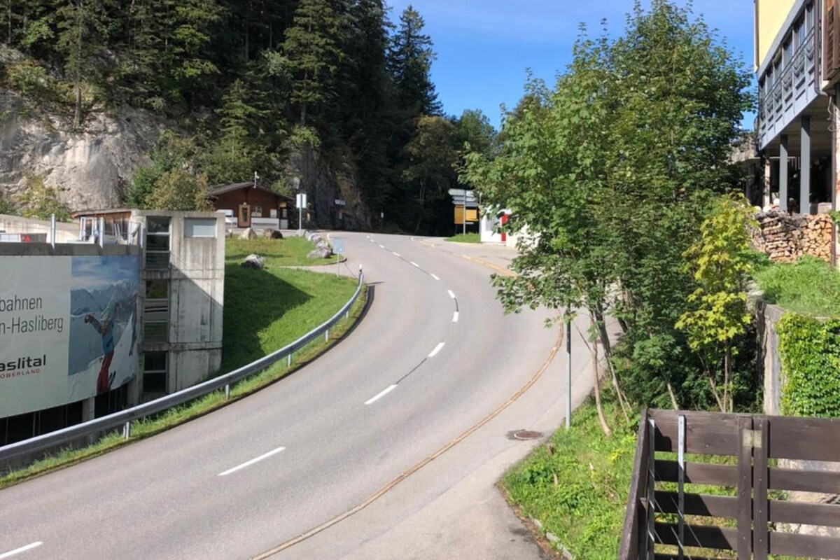 A road curving through a forested area with a building on the right.