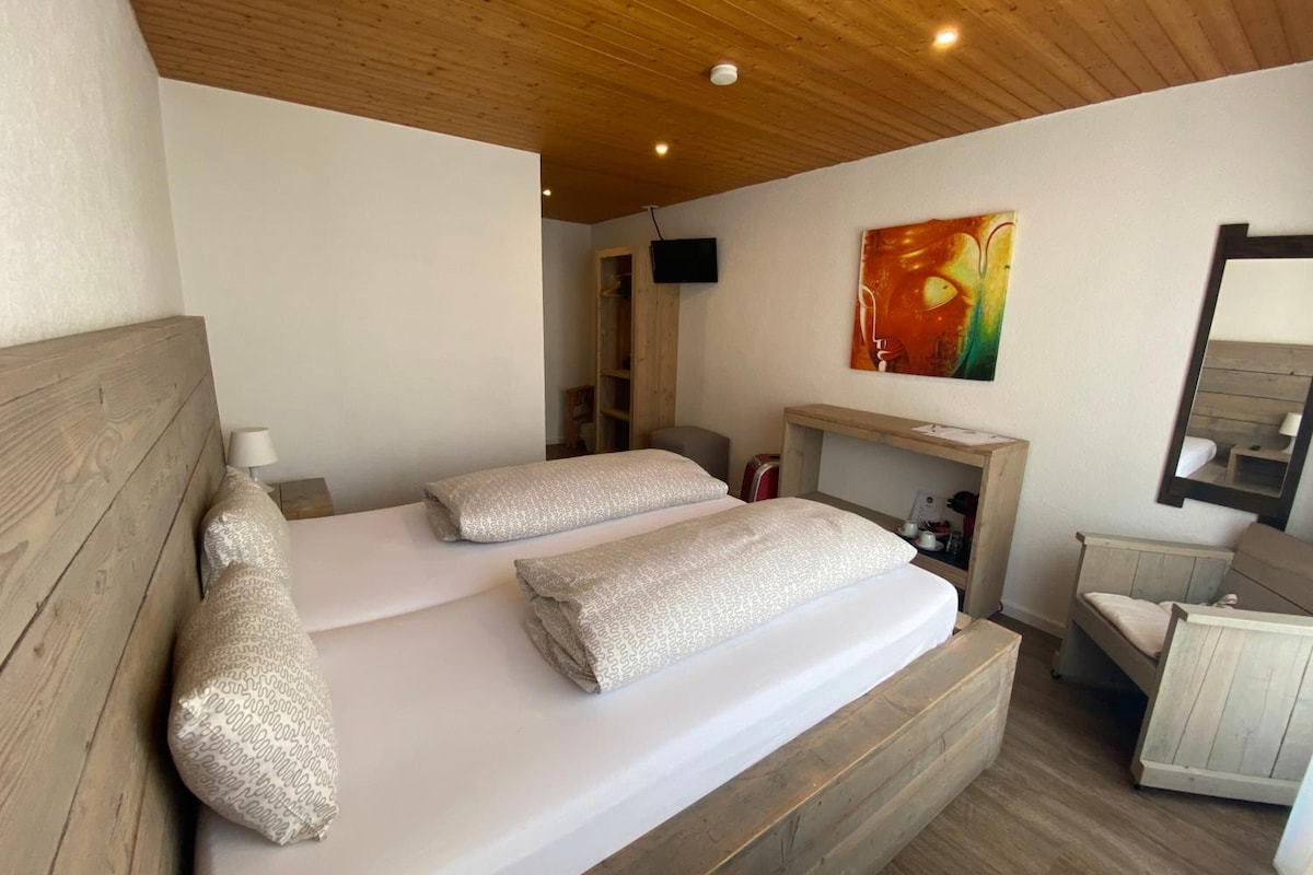 A bedroom with a wooden headboard, a bed with patterned pillows, a bedside table, a mirror, and a painting on the wall.