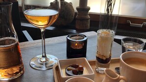 A table with a glass of white wine, a candle, a glass of dark liquid, a cup of coffee, and a tray with nuts and a small bowl of sugar. - Hotel Twing (Hasliberg)