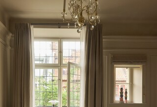 A bedroom with a large bed, a fluffy chair, a bench, and a view of a garden through a window.