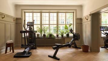 A home gym with exercise equipment, a window with a view of greenery, and a radiator.