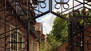 A brick building with a gated entrance, a paved pathway, and well-maintained hedges. - Ett Hem (Stockholm)