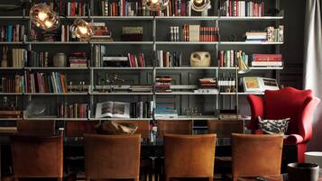 A cozy reading room with a large bookshelf, leather chairs, and a red armchair.