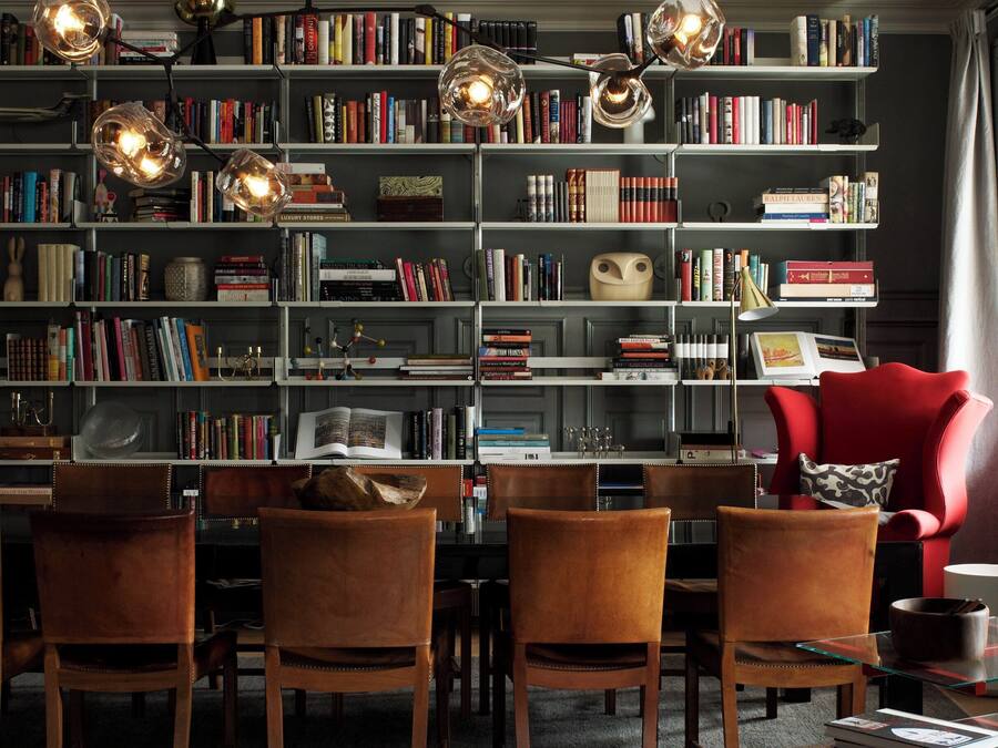 A cozy reading room with a large bookshelf, leather chairs, and a red armchair.