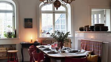 A dining area with a long table set for four, surrounded by red chairs, a potted plant, and a chandelier.