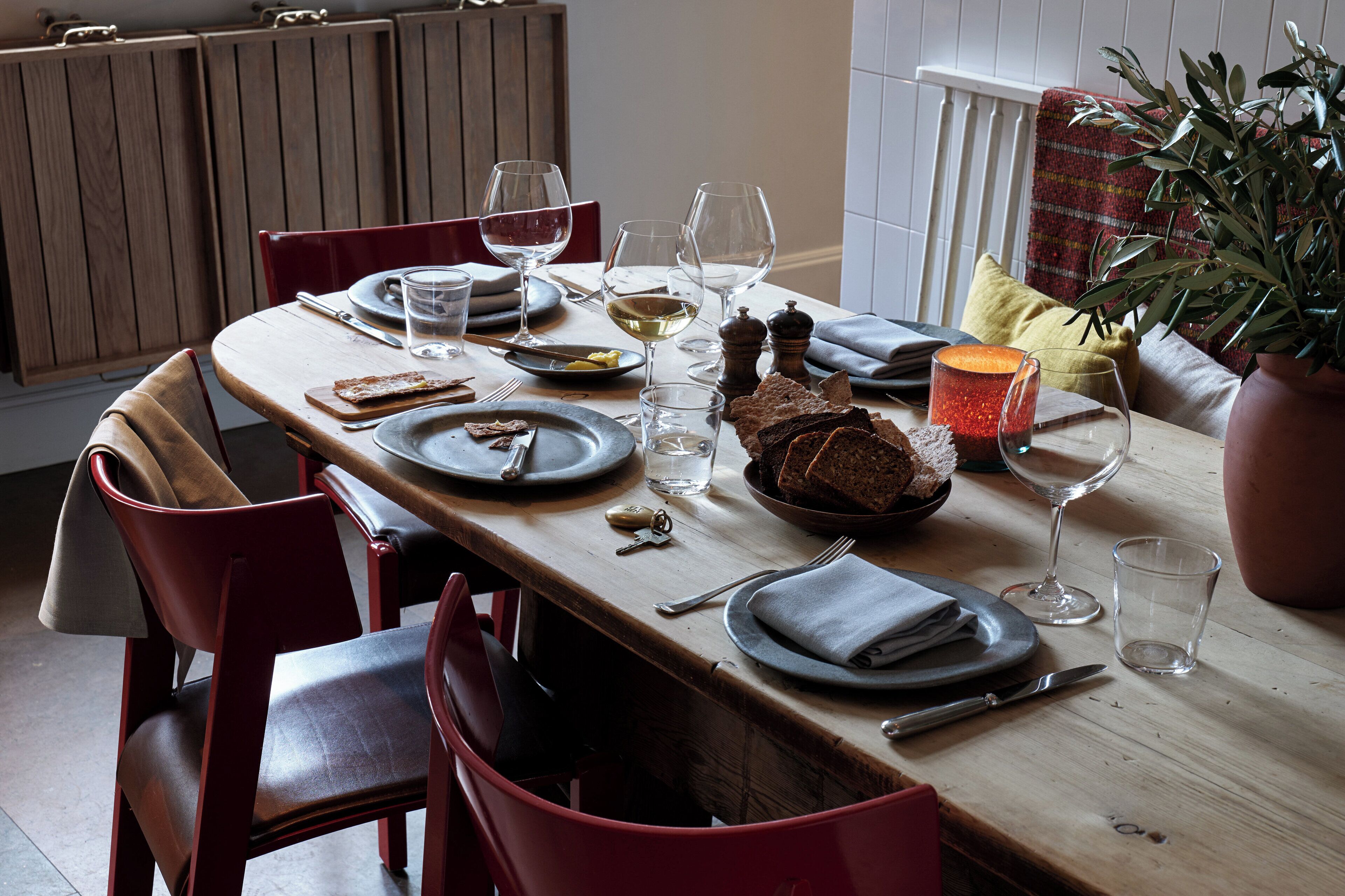 A dining table set with plates, glasses, and cutlery, surrounded by red chairs.