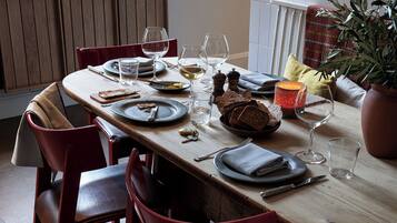 A dining table set with plates, glasses, and cutlery, surrounded by red chairs.