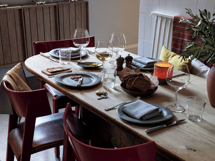 A dining table set with plates, glasses, and cutlery, surrounded by red chairs.