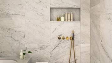 Un baño moderno con pared de mármol, un taburete de madera, una bañera y una ducha con detalles dorados.
