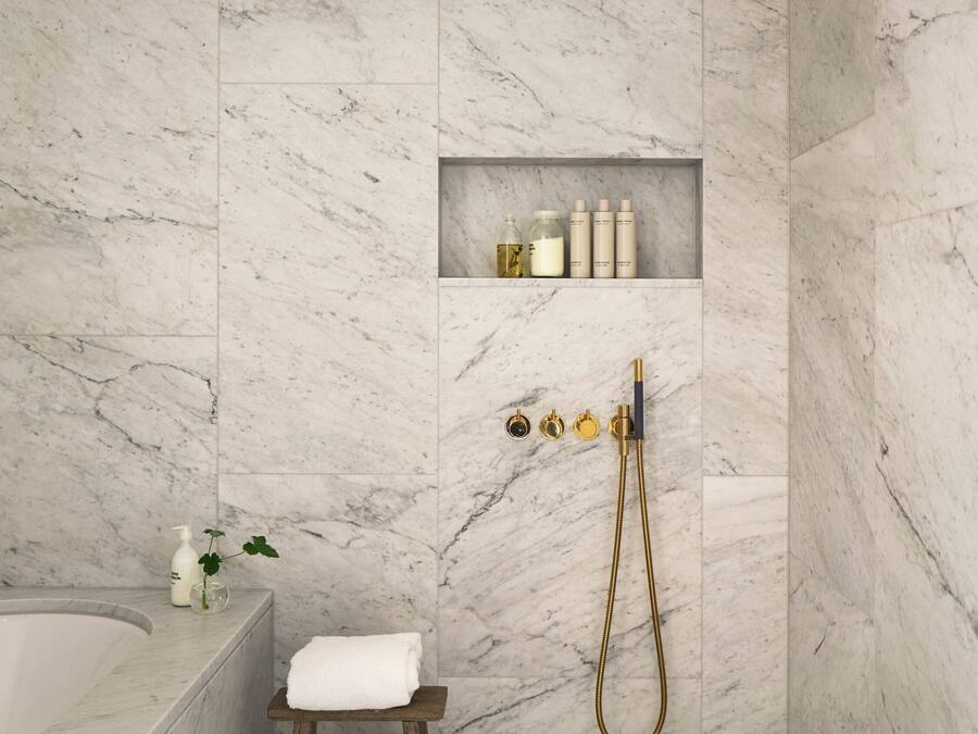 Un baño moderno con pared de mármol, un taburete de madera, una bañera y una ducha con detalles dorados.