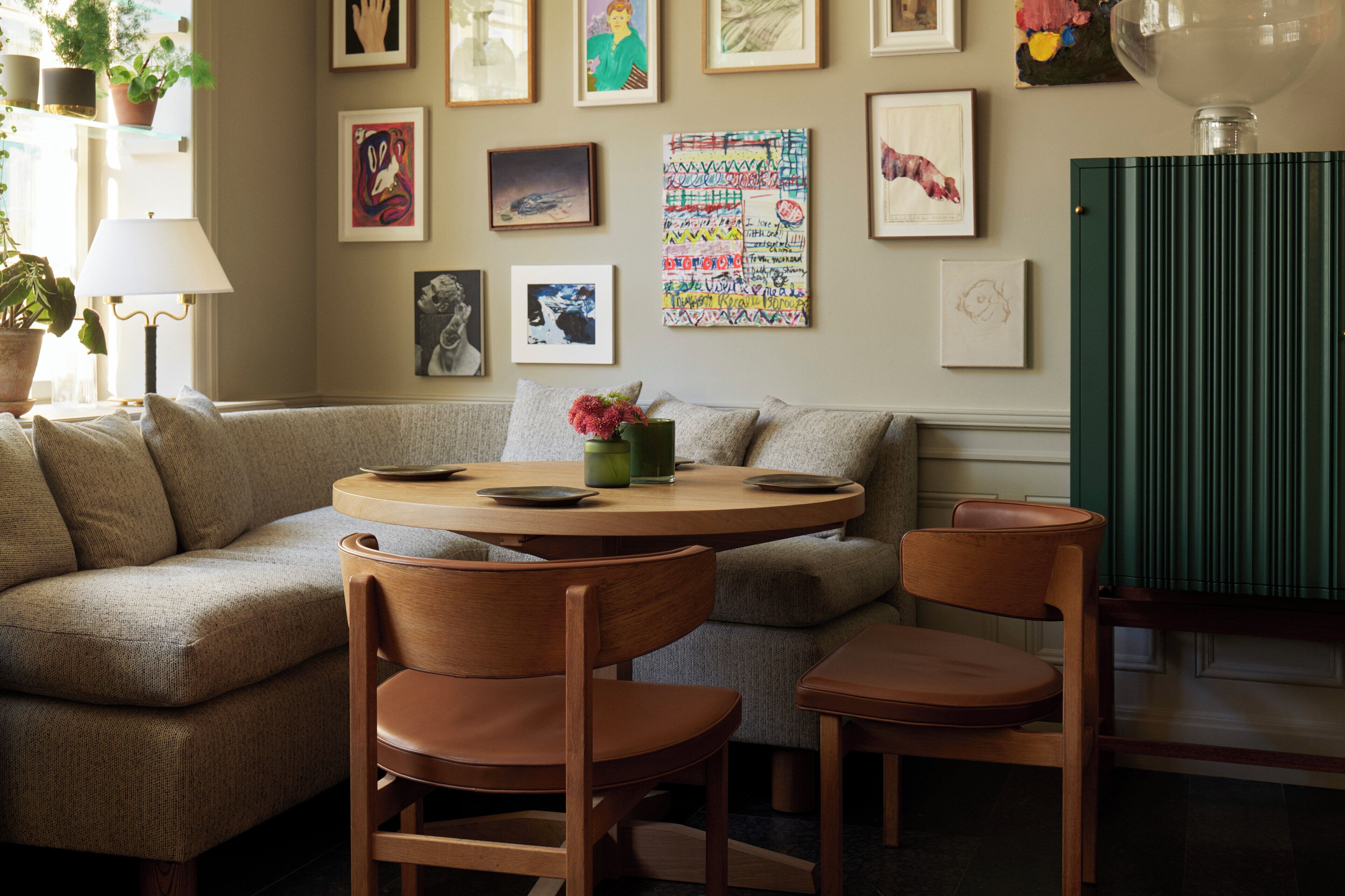 Ein gemütliches Wohnzimmer mit einer Couch, Holzstühlen, einem runden Tisch und verschiedenen gerahmten Kunstwerken an der Wand.