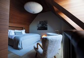 A bedroom with a sloped ceiling, a bed with a headboard, a bedside table, a chair, and a wall-mounted artwork.