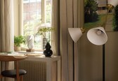 A room with a wooden desk, a chair, a floor lamp, a radiator, and a window with curtains.