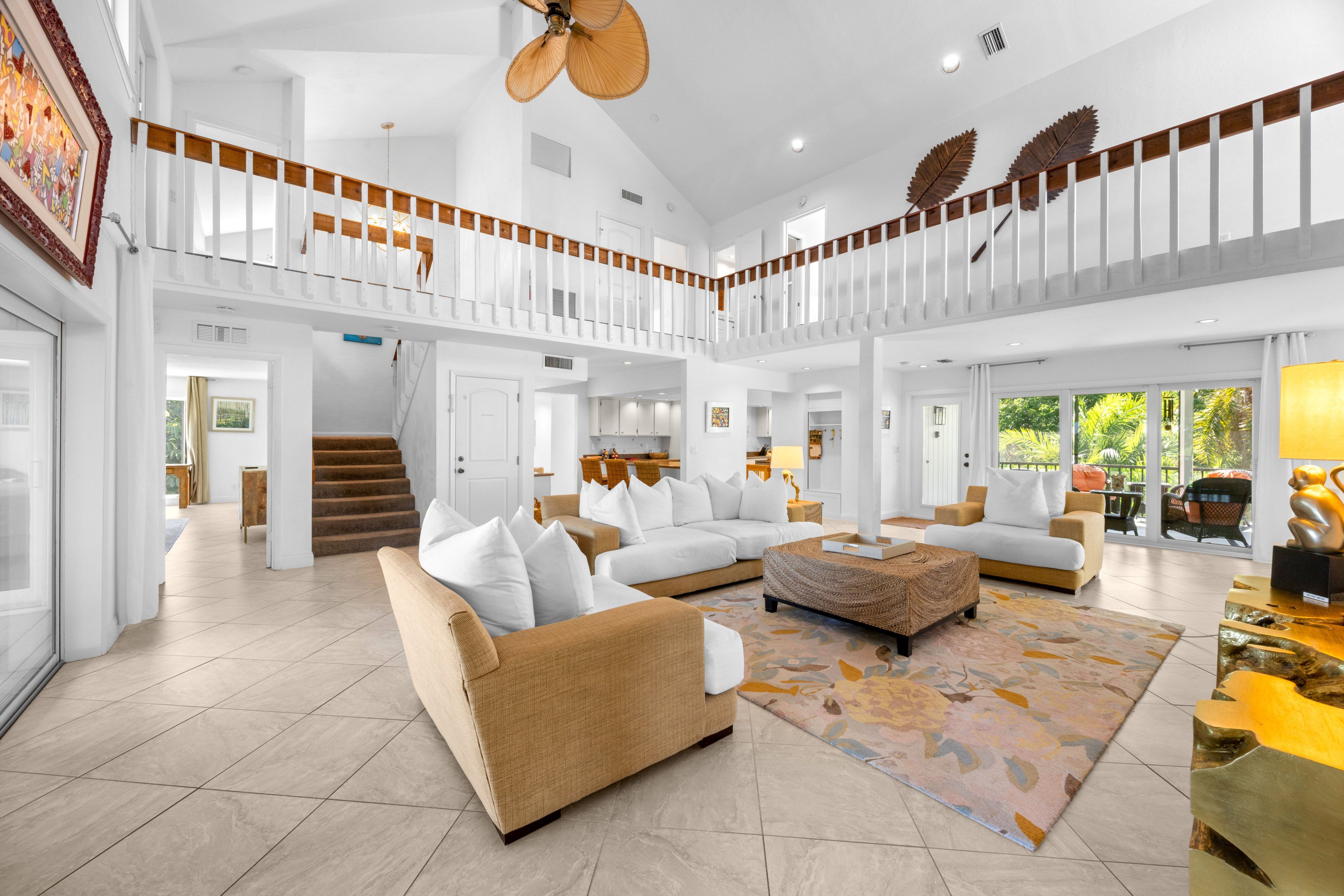 A spacious living area with a high ceiling, a staircase, and a balcony with a view.