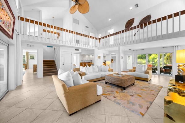 A spacious living area with a high ceiling, a staircase, and a balcony with a view.
