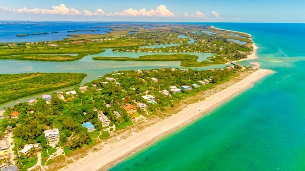 Vista aérea de una zona costera con playa, aguas turquesas cristalinas y algunas casas dispersas.