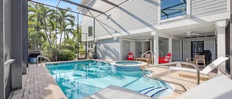 A pool area with a hot tub, lounge chairs, and a covered patio.