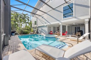 A pool area with a hot tub, lounge chairs, and a covered patio.
