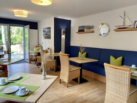 Ein Restaurant mit Holztischen, grünen Kissen und Blick durch große Fenster.