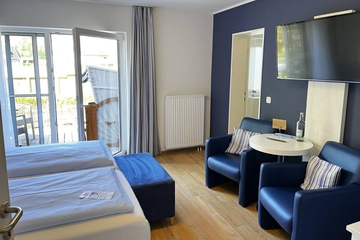 A hotel room with a bed, a seating area with a table, a TV, and a view of the outdoors.