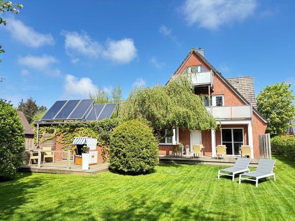 A house with a sloped roof, solar panels, a covered patio, and a well-maintained lawn. - Hotel garni DünenNest (St. Peter-Ording)