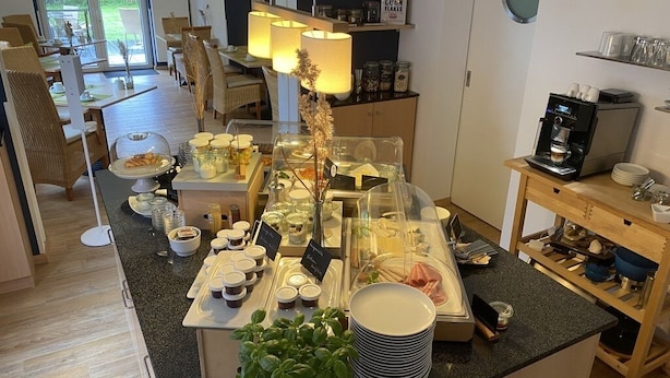 Ein Bereich mit einem Buffet, verschiedenen Speisen, einer Kaffeemaschine und einer Pflanze.
