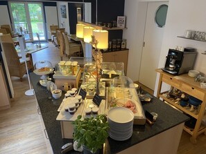A buffet area with various food items, a coffee machine, and a plant. - Hotel garni DünenNest (St. Peter-Ording)