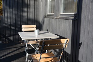 A small outdoor seating area with a table and two wooden chairs, a metal chair, and a white cup on the table.